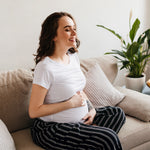 feliz joven embarazada en camiseta blanca en sala estar portada TPNI monogenicas