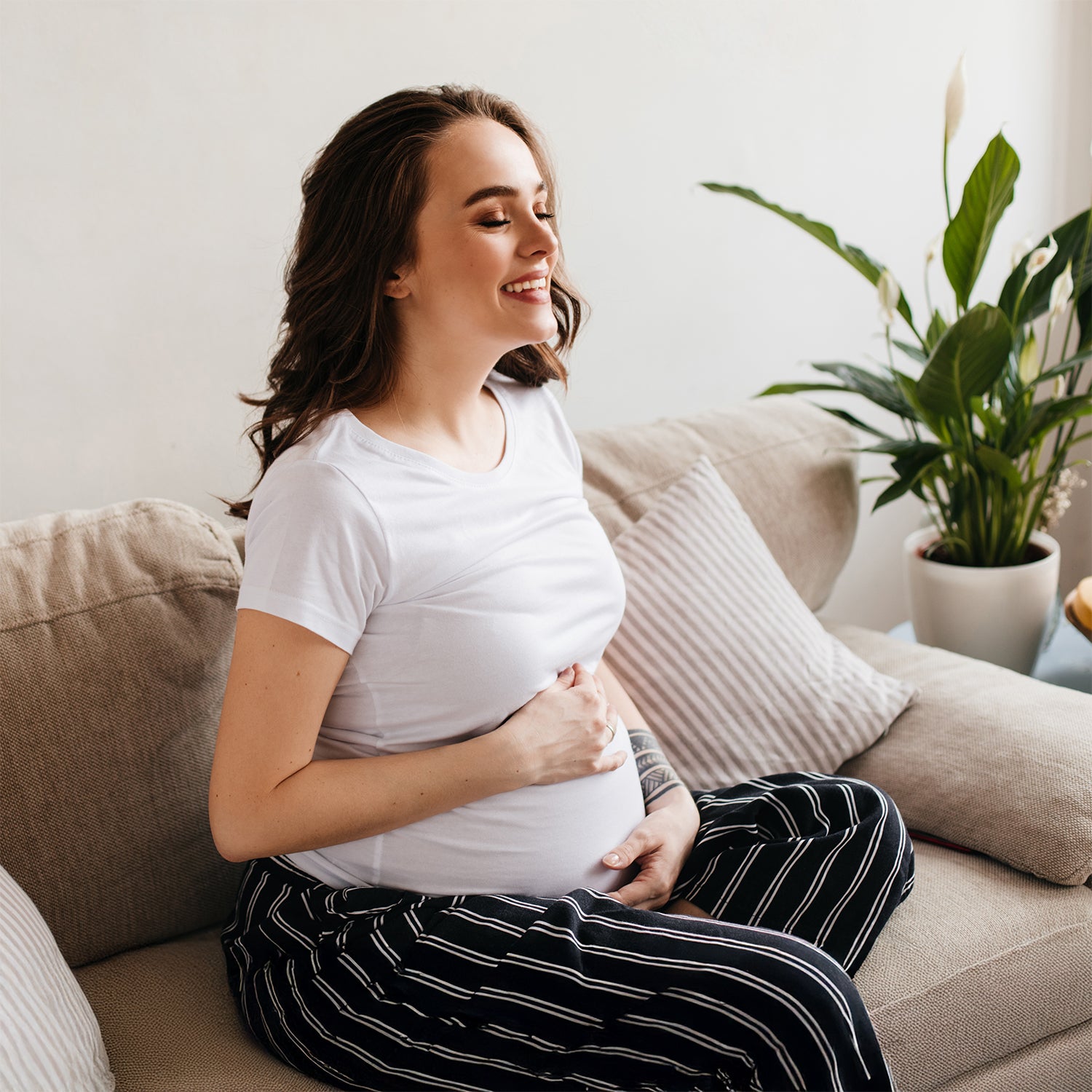 feliz joven embarazada en camiseta blanca en sala estar portada TPNI monogenicas