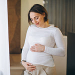 joven embarazada de pie junto la ventana en casa portada TPNI casos especiales PLUS
